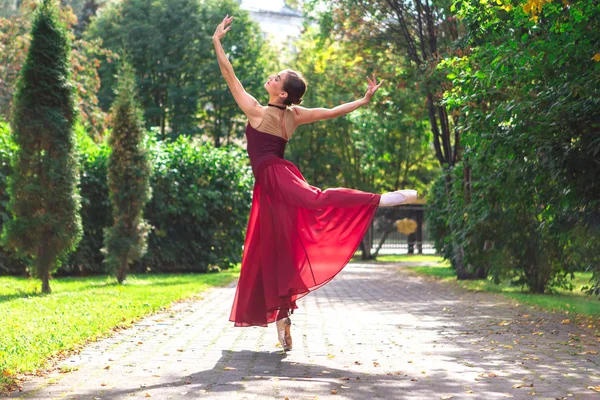 Mulher bailarina em vestido de balé vermelho dançando em sapatos pointe no parque de outono . — Fotografia de Stock