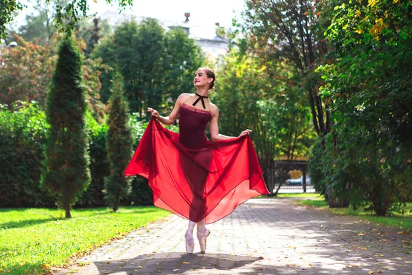 Woman ballerina in red ballet dress dancing in pointe shoes in autumn park.