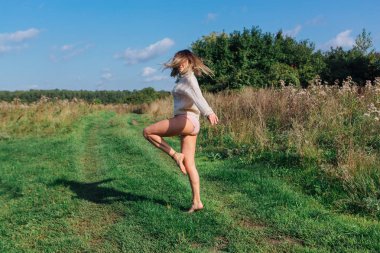 Yeşil bir tarlada çıplak ayakla atlayan genç ve güzel bir kadın.