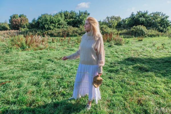 Beautiful blond woman staying and smocking cigarette in a green field