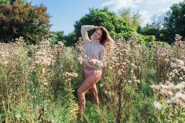 Happy young beautiful woman in sweater and underpants walking with bare foot in a field of dry agrimony — Stock Photo, Image