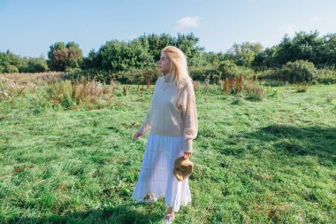 Güzel sarışın kadın kalıyor ve yeşil bir alanda sigara içiyor.