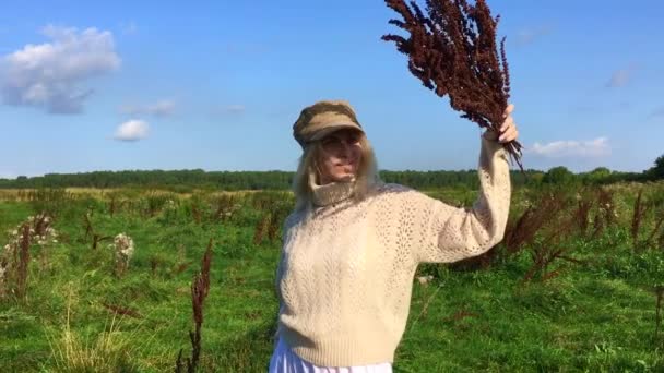 Glad vacker blond kvinna promenader i ett grönt fält med en bukett torra bruna växter — Stockvideo