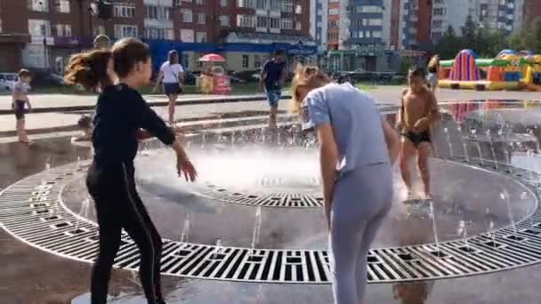 Novokuznetsk, Región de Kemerovo, Rusia - 29 de agosto de 2019: Adolescentes felices salpicando en el agua de una fuente de la ciudad y disfrutando de los frescos arroyos de agua en un día caluroso . — Vídeos de Stock