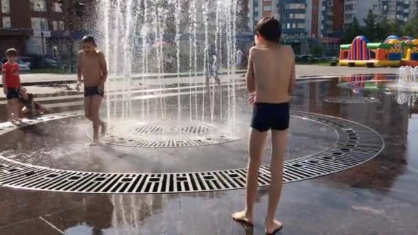 Novokuznetsk, Región de Kemerovo, Rusia - 29 de agosto de 2019: Adolescentes felices salpicando en el agua de una fuente de la ciudad y disfrutando de los frescos arroyos de agua en un día caluroso . — Vídeo de stock