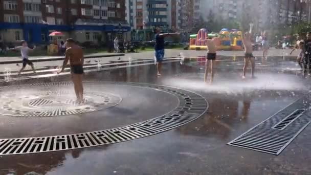 Novokuznetsk, Región de Kemerovo, Rusia - 29 de agosto de 2019: Adolescentes felices salpicando en el agua de una fuente de la ciudad y disfrutando de los frescos arroyos de agua en un día caluroso . — Vídeos de Stock