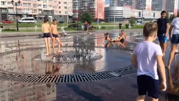 Novokuznetsk, Región de Kemerovo, Rusia - 29 de agosto de 2019: Adolescentes felices salpicando en el agua de una fuente de la ciudad y disfrutando de los frescos arroyos de agua en un día caluroso . — Vídeos de Stock