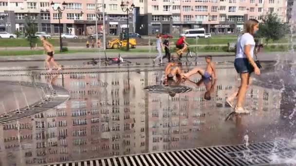 Novokuznetsk, région de Kemerovo, Russie - 29 août 2019 : Des adolescents heureux éclaboussent dans l'eau d'une fontaine de la ville et profitent des flux d'eau frais lors d'une journée chaude . — Video