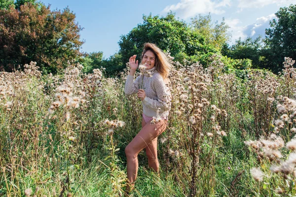 Happy young beautiful woman in sweater and underpants walking with bare foot in a field of dry agrimony — Stock Photo, Image