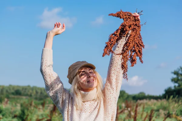 Glücklich schöne blonde Frau zu Fuß in einem grünen Feld mit einem Strauß trockener brauner Pflanzen — Stockfoto