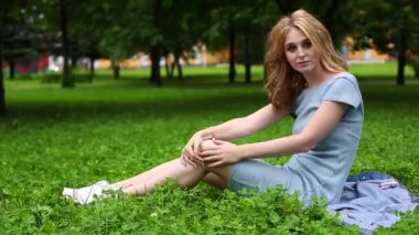 Genç ve güzel bir kız bulutlu bir günde çimenlerde oturuyor, gülümsüyor, rahatlıyor, konsept kuruyor, hayal kuruyor.