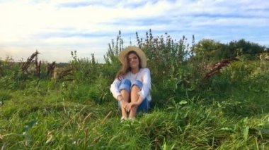 Mutlu güzel esmer genç kız çimlerin üzerinde oturuyor, gülümsüyor ve saçlarına dokunuyor.