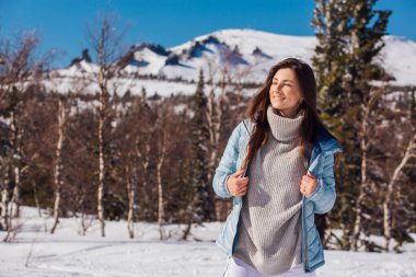 Kışın karlı dağ manzarasında mavi gözlü ve yüzünde çiller olan güzel esmer bir kadının portresi. Kışın açık havada güzel bir kız.