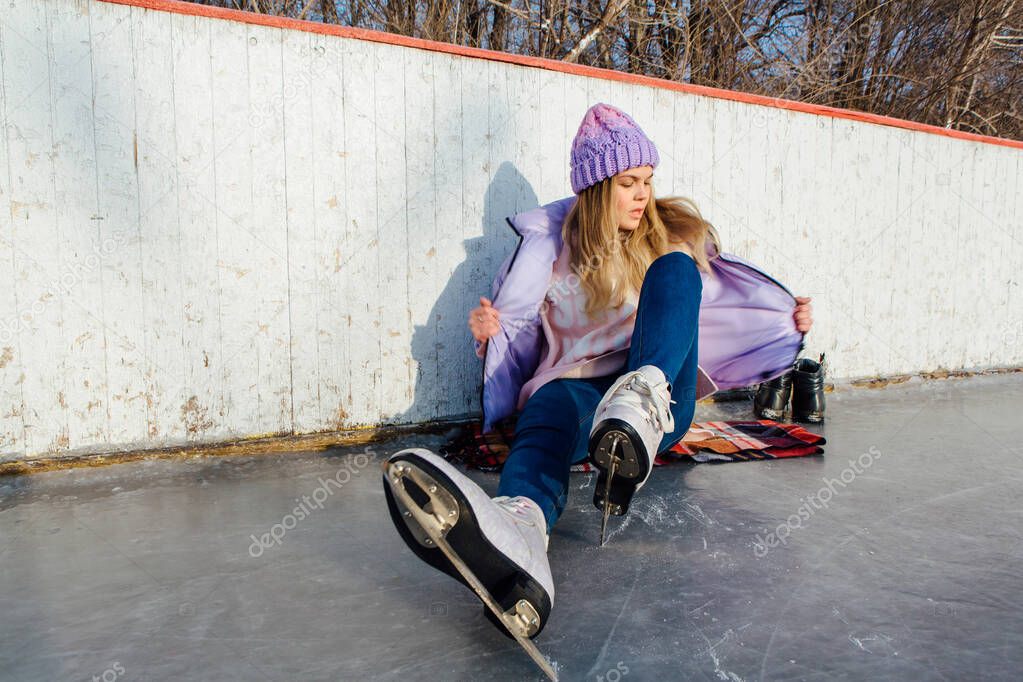 Lovely young woman sitting on ice ring and tieing shoelaces