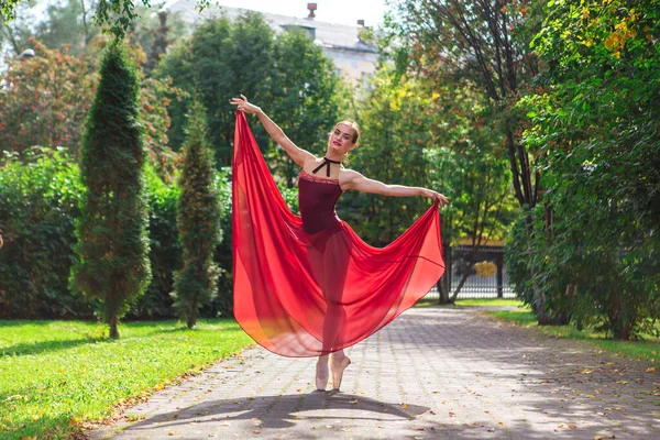 Bailarina de mujer en vestido de ballet rojo bailando en zapatos puntiagudos en el parque de otoño . — Foto de Stock