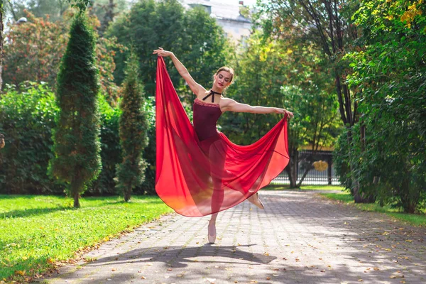Bailarina de mujer en vestido de ballet rojo bailando en zapatos puntiagudos en el parque de otoño . — Foto de Stock