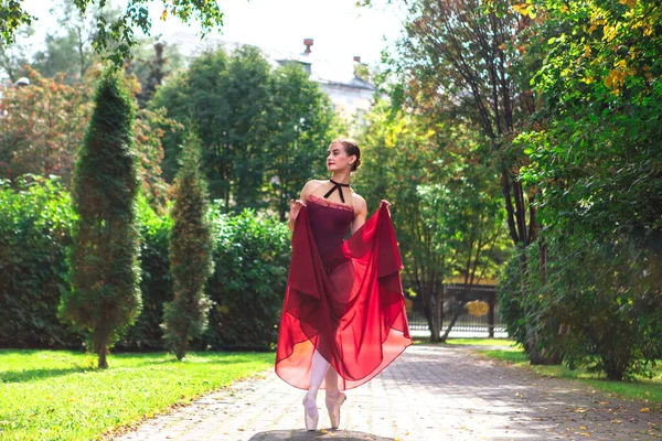 Bailarina de mujer en vestido de ballet rojo bailando en zapatos puntiagudos en el parque de otoño . — Foto de Stock