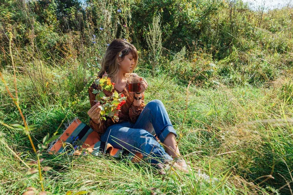 Bella donna con fiore di camomilla in capelli e un ramo di bacca di viburno seduto sull'erba e bere tè all'aperto — Foto Stock