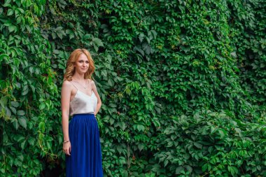 Vahşi üzüm yapraklarının yanında duran genç ve güzel bir kadının portresi..