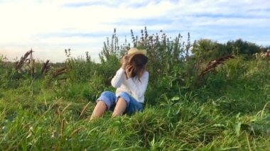 Mutlu güzel esmer genç kız çimlerin üzerinde oturuyor, gülümsüyor ve saçlarına dokunuyor.