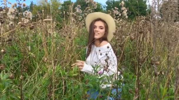 Feliz hermosa morena adolescente sentada en la hierba, sonriendo y tocándose el pelo — Vídeos de Stock