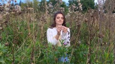 Mutlu güzel esmer genç kız çimlerin üzerinde oturuyor, gülümsüyor ve saçlarına dokunuyor.