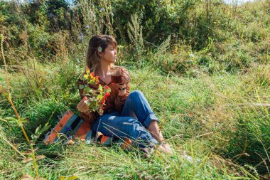 Saçında papatya çiçeği olan güzel bir kadın ve çimlerin üzerinde oturmuş dışarıda çay içen bir viburyum dutu dalı.