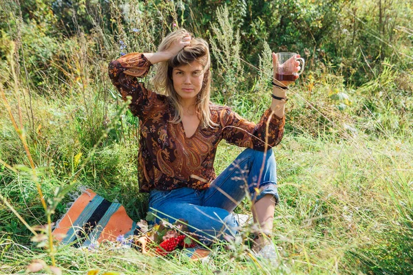 Красивая женщина сидит на траве и пьет чай на открытом воздухе — стоковое фото