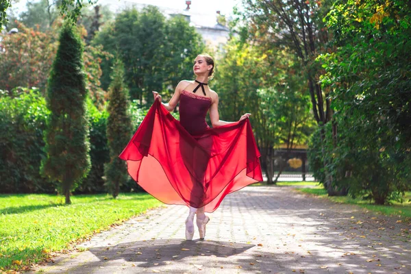 Vrouw ballerina in rood ballet jurk dansen in pointe schoenen in de herfst park. — Stockfoto