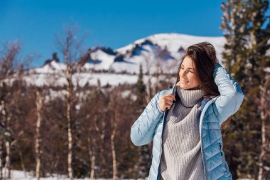 Kışın karlı dağ manzarasında mavi gözlü ve yüzünde çiller olan güzel esmer bir kadının portresi. Kışın açık havada güzel bir kız.