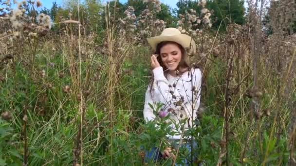 Feliz bela morena adolescente sentada na grama, sorrindo e tocando seu cabelo — Vídeo de Stock