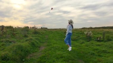 Yeşil bir tarlada yürüyen güzel, esmer, mutlu bir genç kız. Renkli gökyüzü ile güzel bir gün batımında. Paraglider 'a el sallayan kız