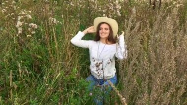 Mutlu güzel esmer genç kız çimlerin üzerinde oturuyor, gülümsüyor ve saçlarına dokunuyor.