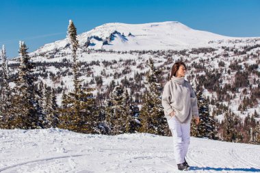 Kışın karlı dağ manzarasında mavi gözlü ve yüzünde çiller olan güzel esmer bir kadının portresi. Kışın açık havada güzel bir kız.