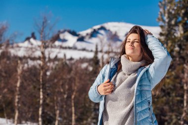 Kışın karlı dağ manzarasında mavi gözlü ve yüzünde çiller olan güzel esmer bir kadının portresi. Kışın açık havada güzel bir kız.