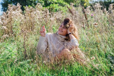 Kuru tarlada çıplak ayakla oturan süveter ve iç çamaşırlı mutlu genç bir kadın.
