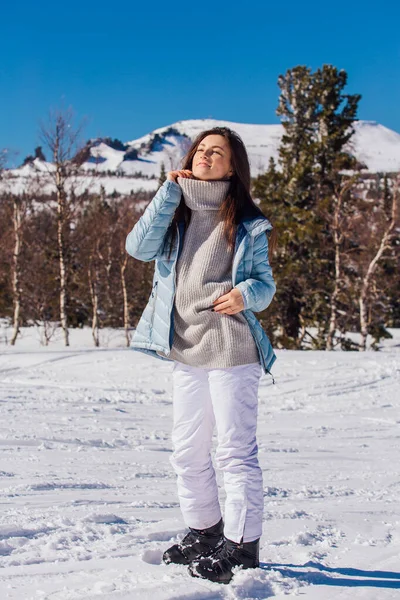 Porträtt av en ung vacker brunett kvinna med blå ögon och fräknar i ansiktet i vinter snöiga bergslandskap. Vacker flicka på vintern utomhus. — Stockfoto