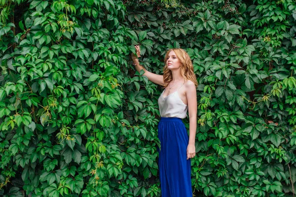 Retrato de una joven mujer hermosa, de pie junto a la pared de hojas de uva silvestre . — Foto de Stock