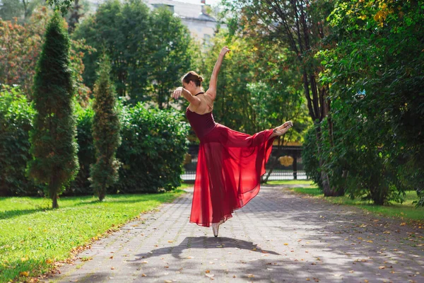 Woman ballerina in red ballet dress dancing in pointe shoes in autumn park.