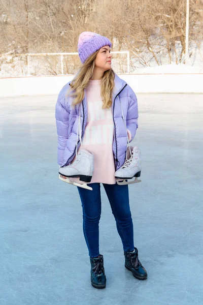 Lovely young woman with ice skates hanging on neck on the ice rink.