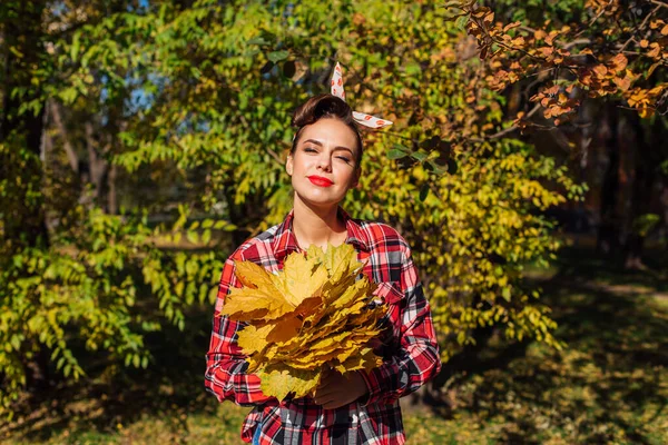 Beautiful woman with make up and hair in pin up holding big bouquet of maple yellow leaves. — Stock Photo, Image