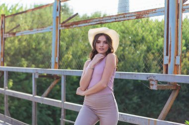 Gün batımında eski paslı köprüde poz veren kovboy şapkası takan güzel genç bir kadın..