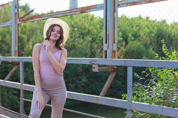 Mujer joven y bonita con sombrero de vaquero posando en el viejo puente oxidado durante la puesta del sol . — Foto de Stock