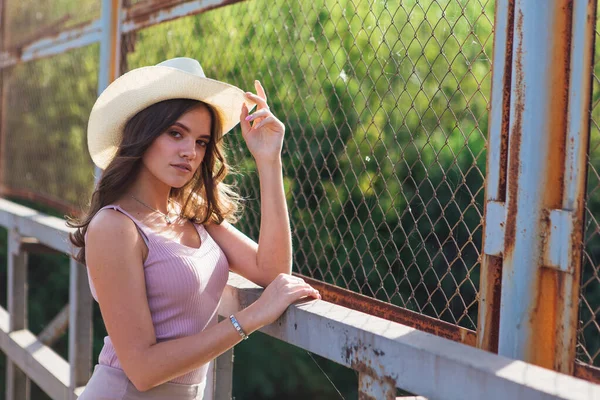 해질 녘낡은 다리 위에서 카우보이 모자를 쓰고 있는 예쁜 젊은 여자. — 스톡 사진