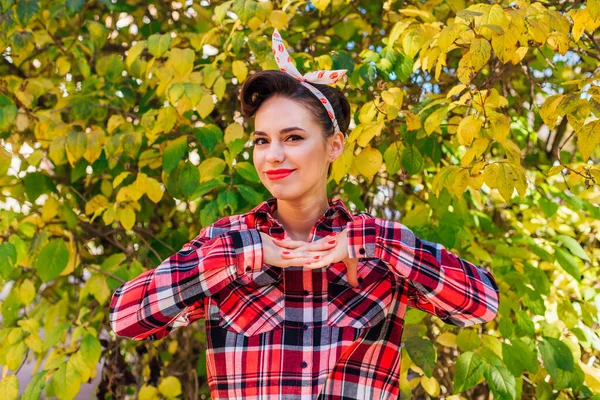 Krásná žena s make-upem a vlasy v pin up stylu stojící vedle podzimního keře — Stock fotografie
