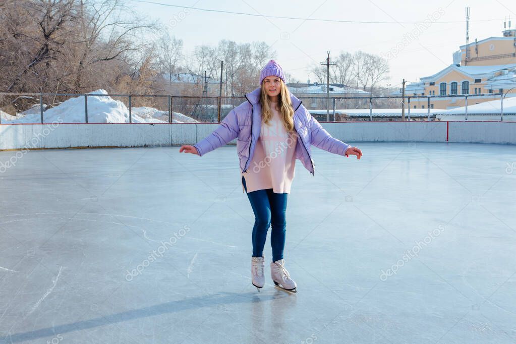 Lovely young woman with riding ice skates on the ice rink.