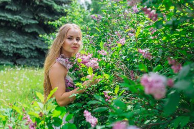 Leylak çalıyanında duran güzel beyaz elbise giyen büyüleyici sarışın bir kadın portresi.