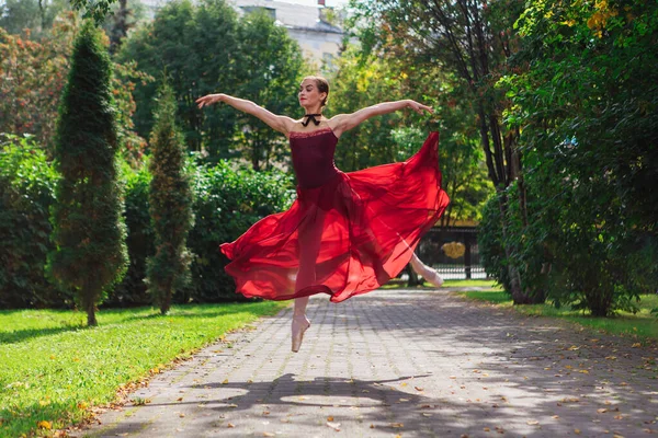 Bailarina de mujer en vestido de ballet rojo bailando en zapatos puntiagudos en el parque de otoño . —  Fotos de Stock