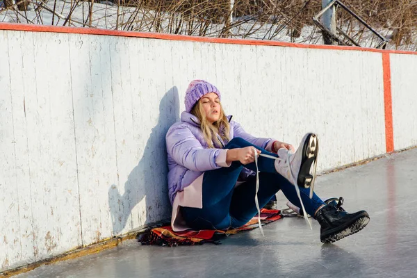 Preciosa joven sentada en un anillo de hielo y atando cordones — Foto de Stock