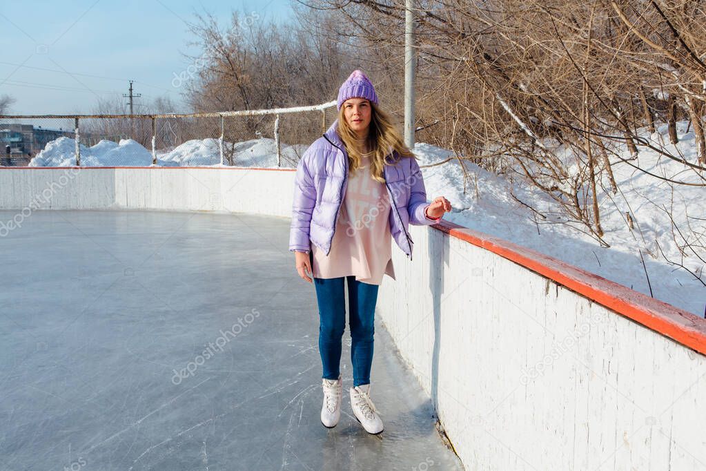 Lovely young woman with riding ice skates on the ice rink.